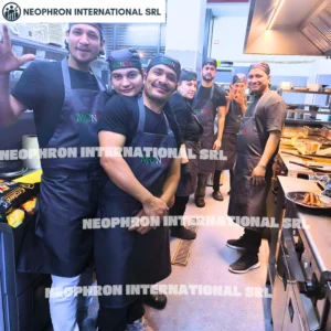 A team of chefs and kitchen staff wearing professional uniforms and aprons pose together inside a busy commercial kitchen, showing teamwork and hands-on experience in the hospitality industry.